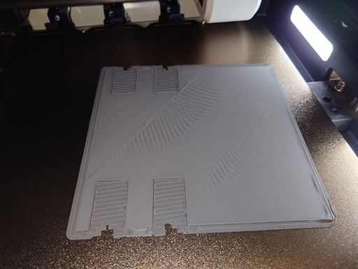 A photo of a 3d printer plate with a partially finished square print on it. the middle of the print has very pronounced wrinkling on the flat layer.